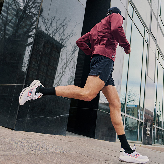 A person running on a sidewalk wearing Saucony shoes.