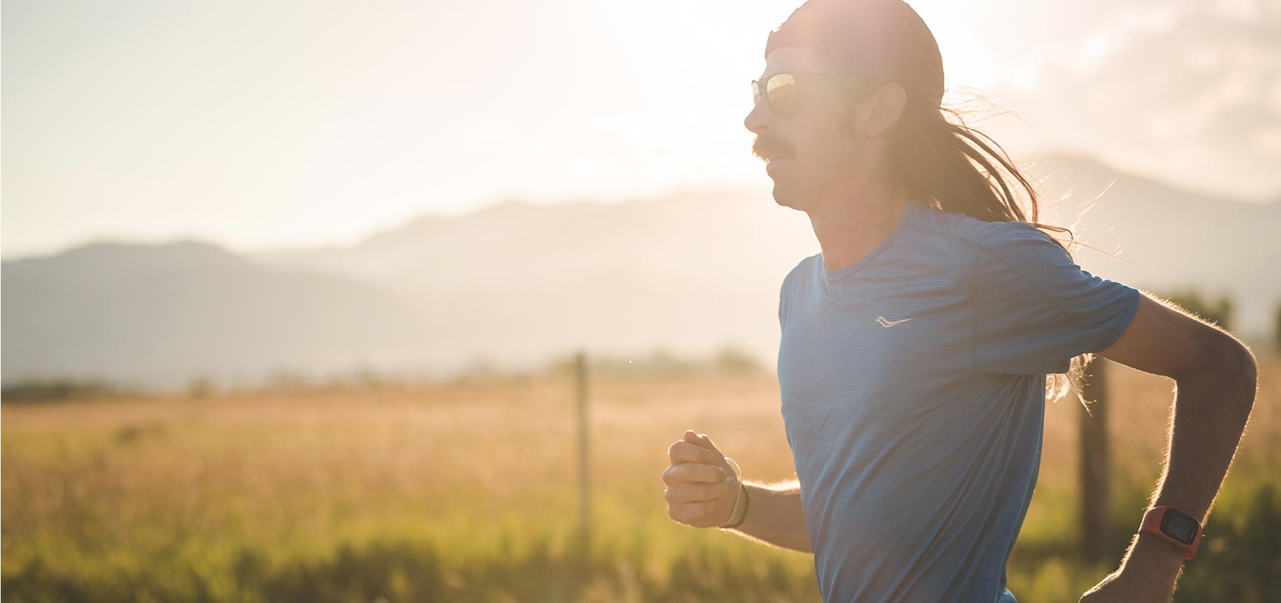 Noah Droddy running wearing a blue Saucony shirt with the sun gazing behind him.