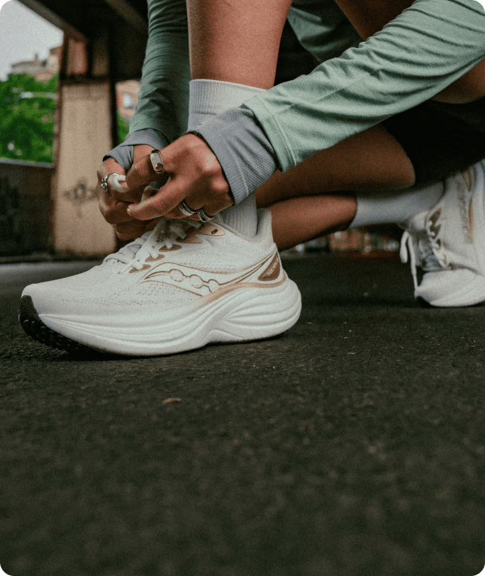 Gros plan sur les pieds d'une personne portant des chaussures Saucony Triumph 24, debout sur un trottoir avant une course.