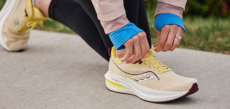 A person tying a shoelace on Saucony shoes.