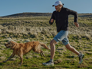 A person running with a dog on a trail wearing Saucony shoes.
