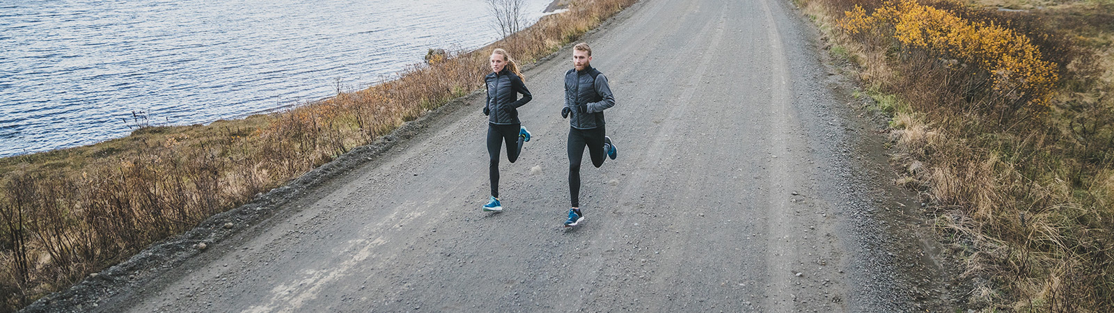 A male and female running on a dirt road next to a body of water.