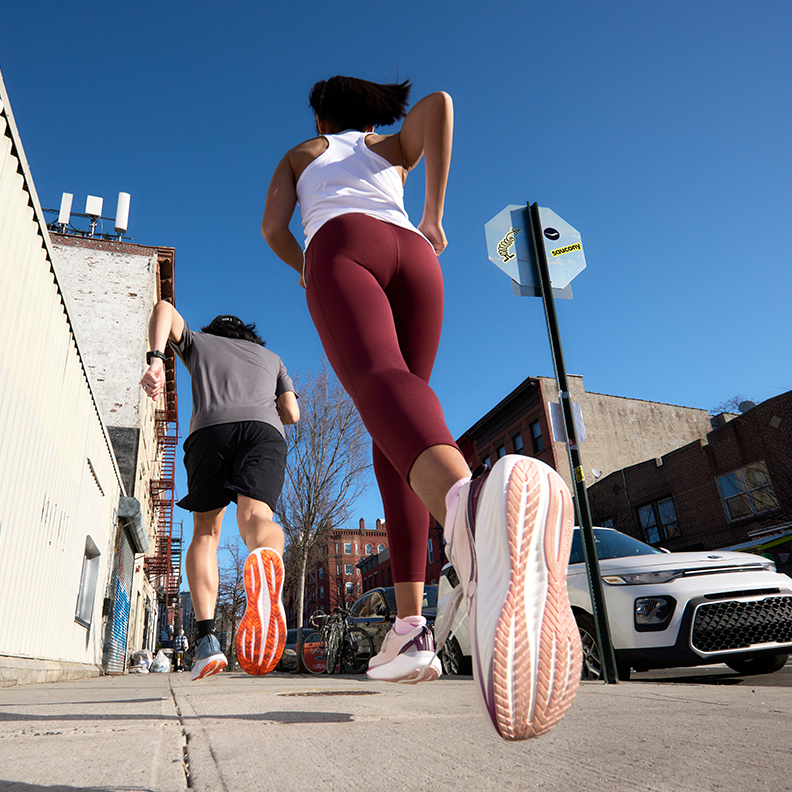 Two people running on a sidewalk wearing Saucony running shoes.