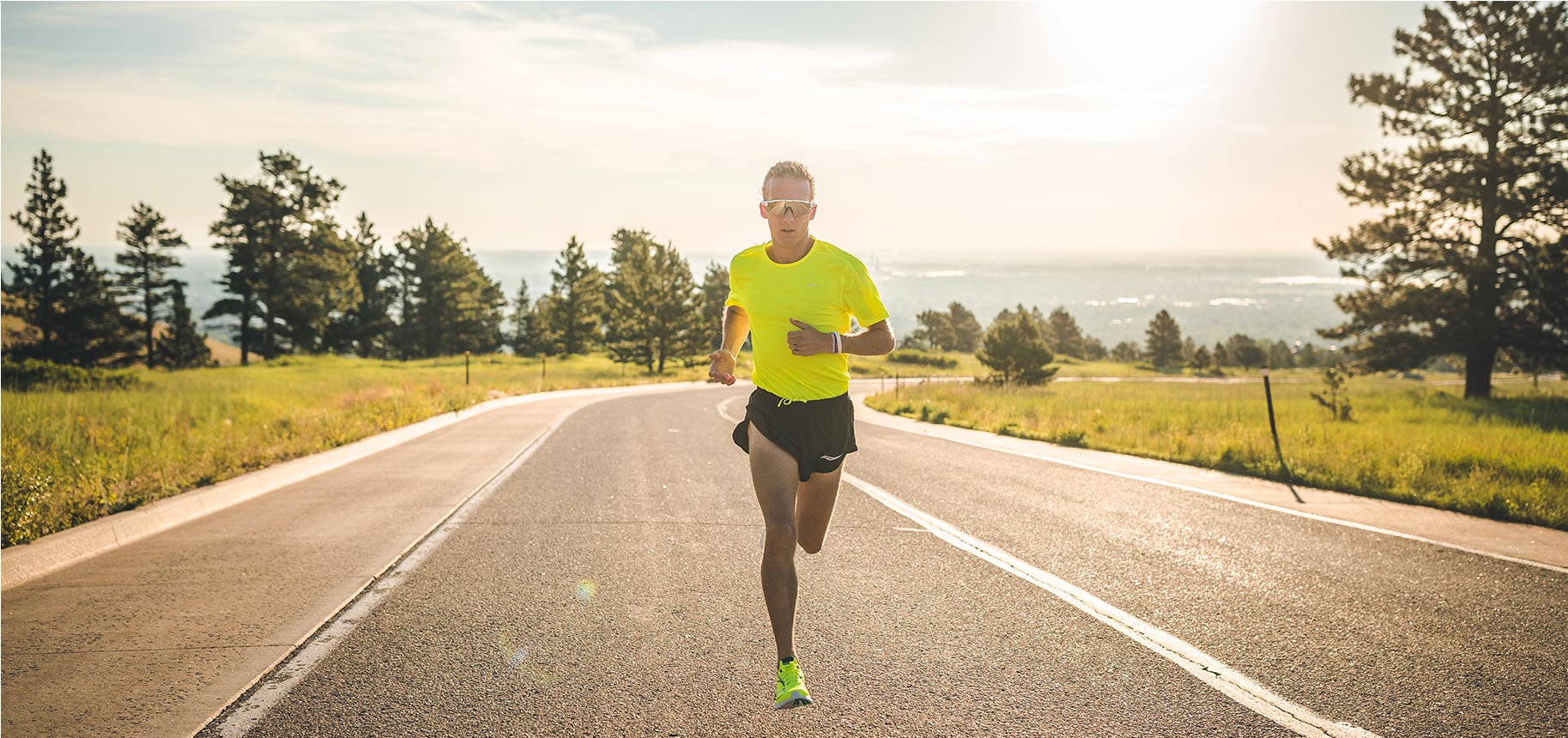 Parker Stinson running in green Saucony shoes and neon yellow t-shirt down a long and winding road.