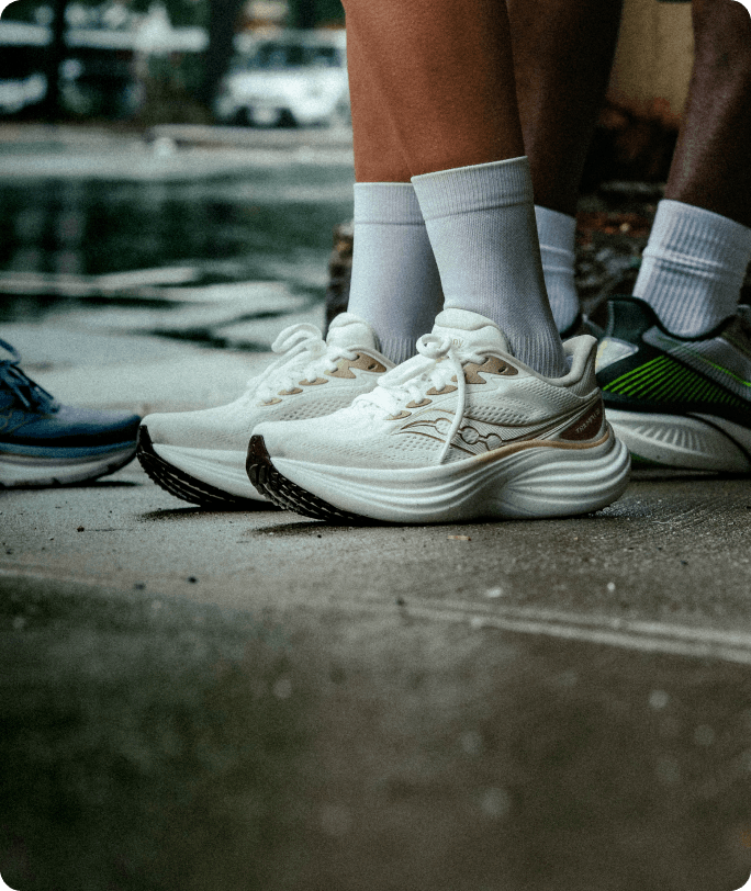 Gros plan sur les pieds d'une personne portant des chaussures Saucony Triumph 24, debout sur un trottoir avant une course.