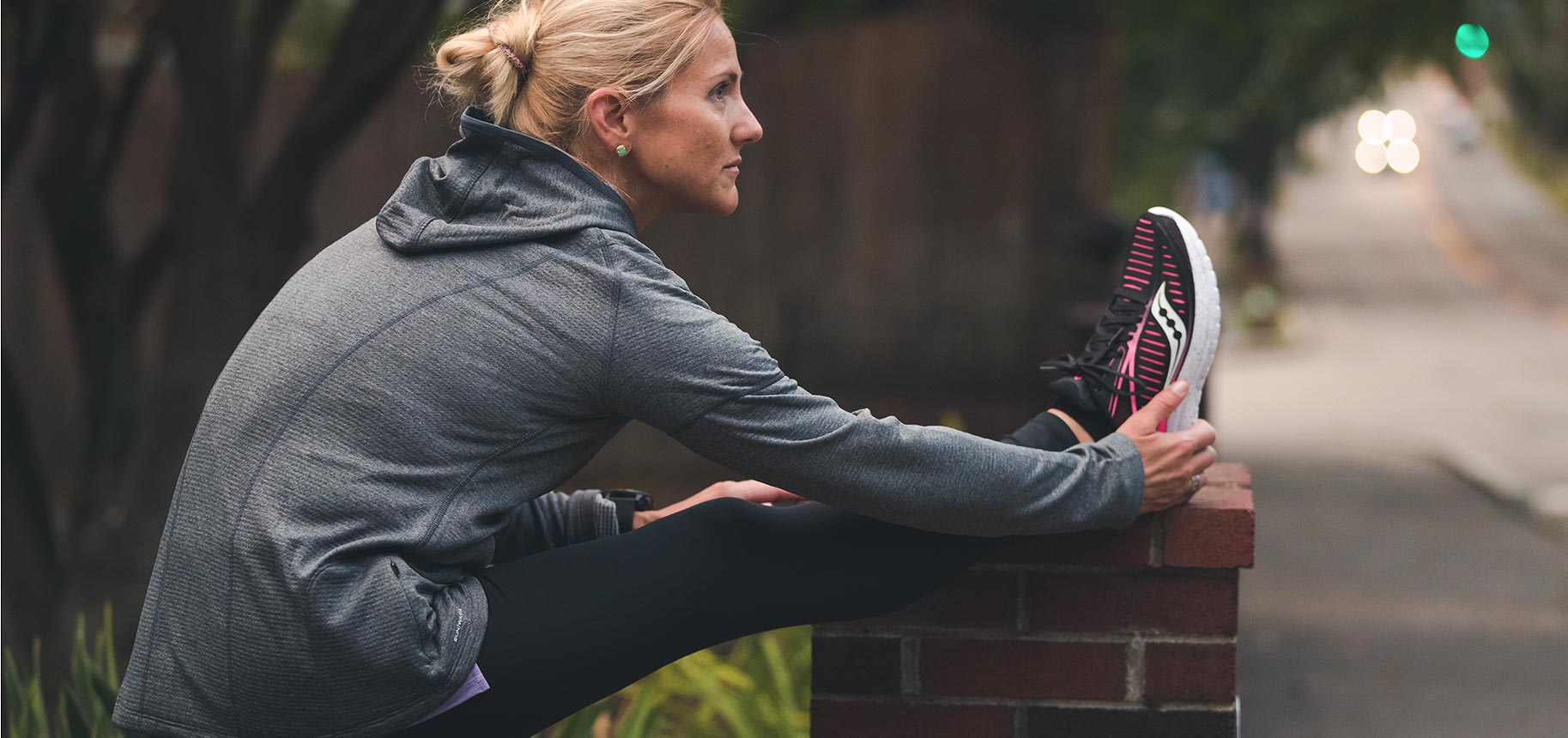 Katie Crowell stretching her leg on a brick wall.