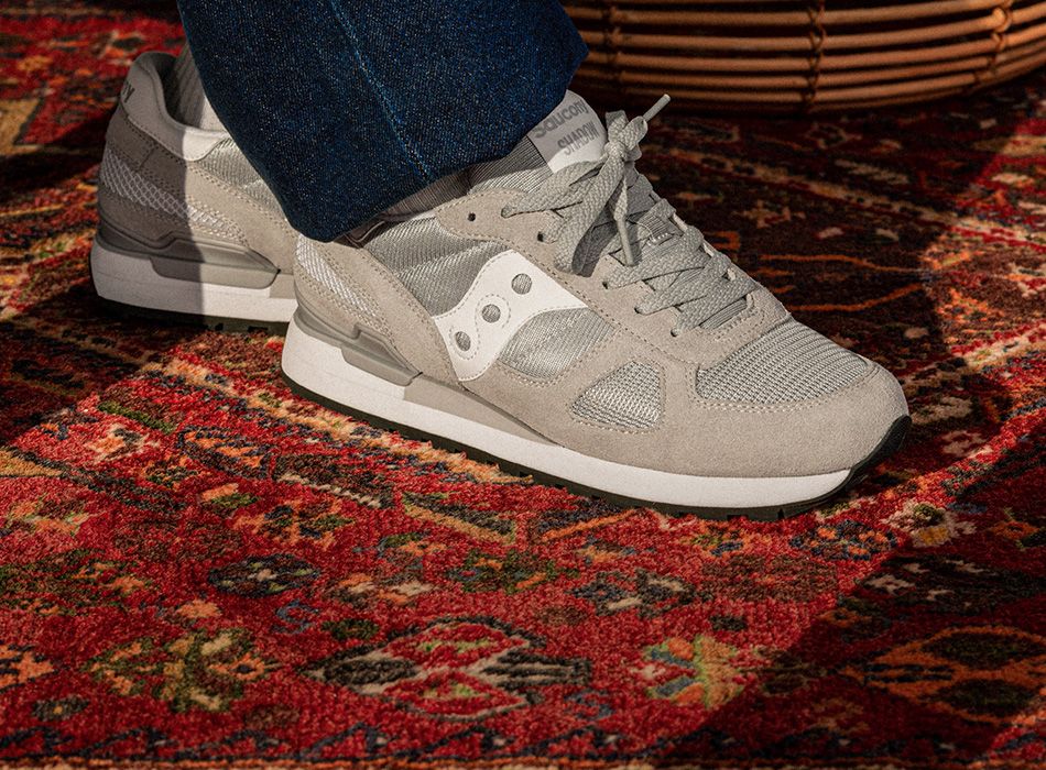 A person's feet in a grey and white Saucony Originals shoes.