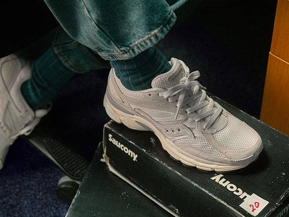 A person's foot wearing white Saucony shoe on a box.
