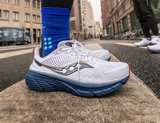 Les pieds d'une personne portant des chaussures de course Saucony blanches et des chaussettes bleues sur un trottoir.