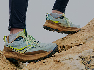 A person's feet in Saucony shoes on rocks.