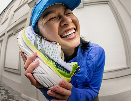 A woman holding a Saucony shoe and smiling.