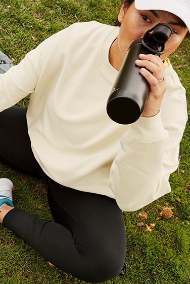 A person sitting on the ground drinking from a bottle.