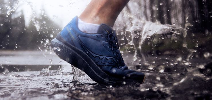Le pied d'une personne portant des chaussures Saucony dans une flaque d'eau.