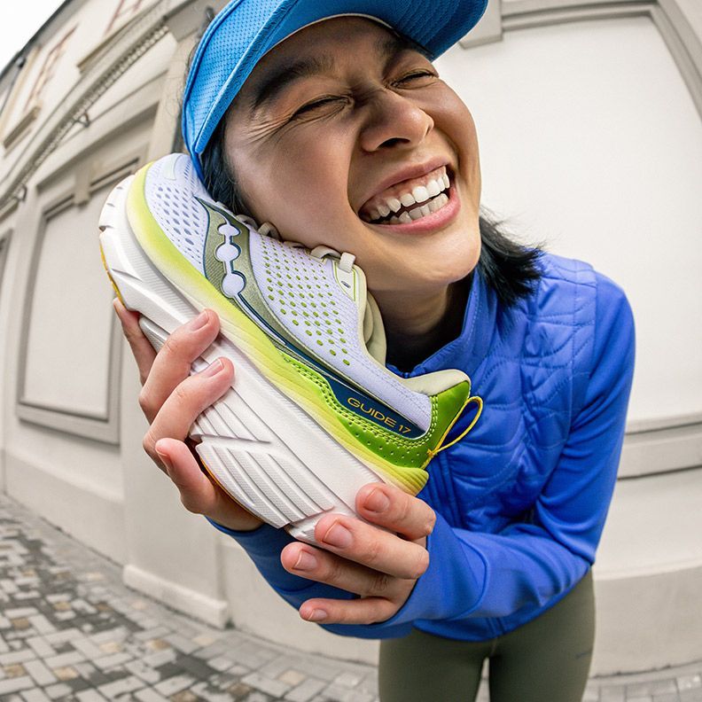 A person holding a Saucony Guide 17 running shoe and smiling.