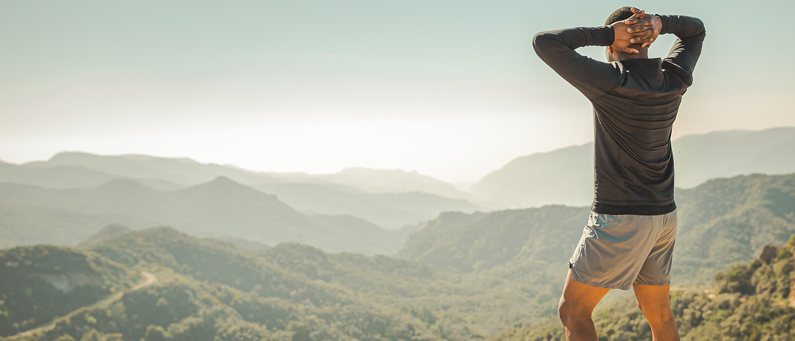 Person stands on a hill looking at distant mountains.