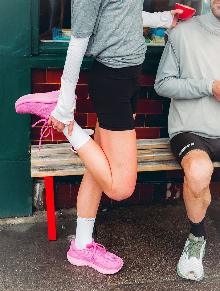 a woman stretching her leg while a man sits on a bench