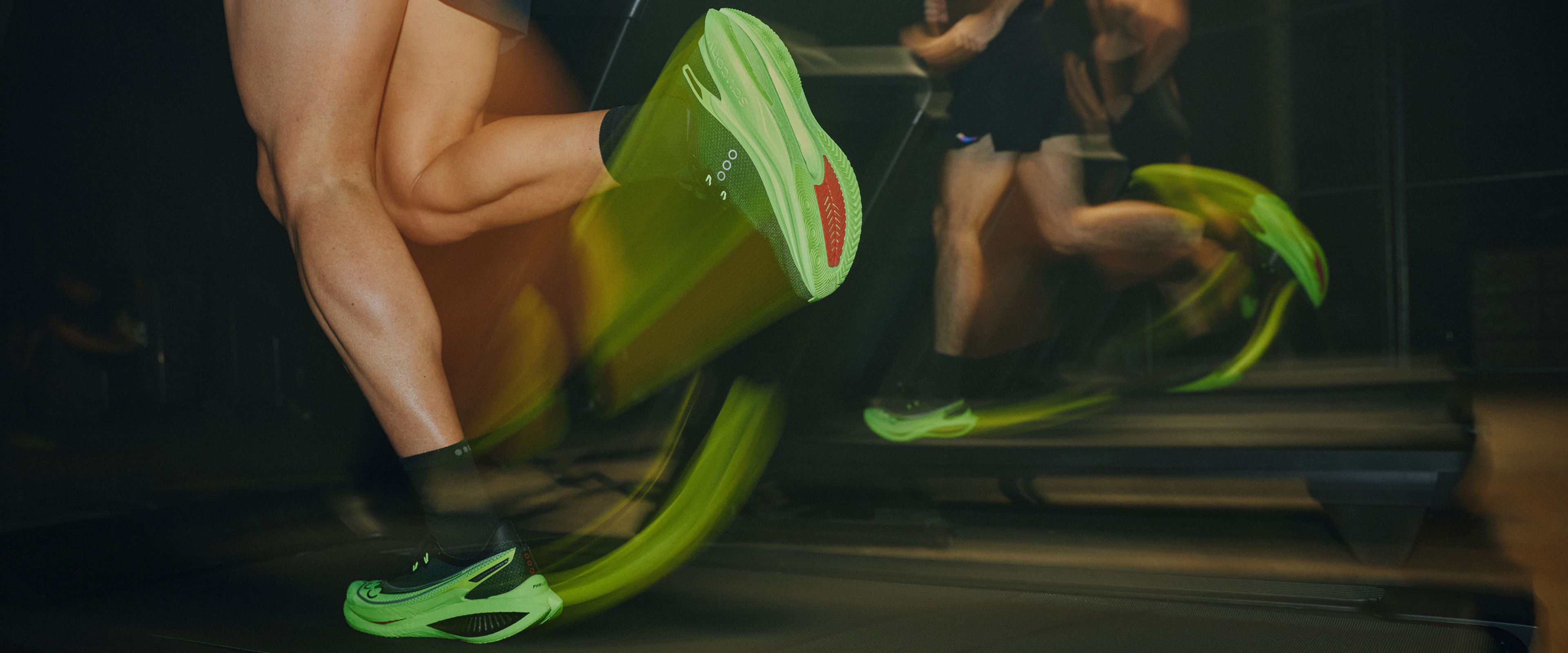 Runners wearing bright green Saucony running shoes on treadmills.