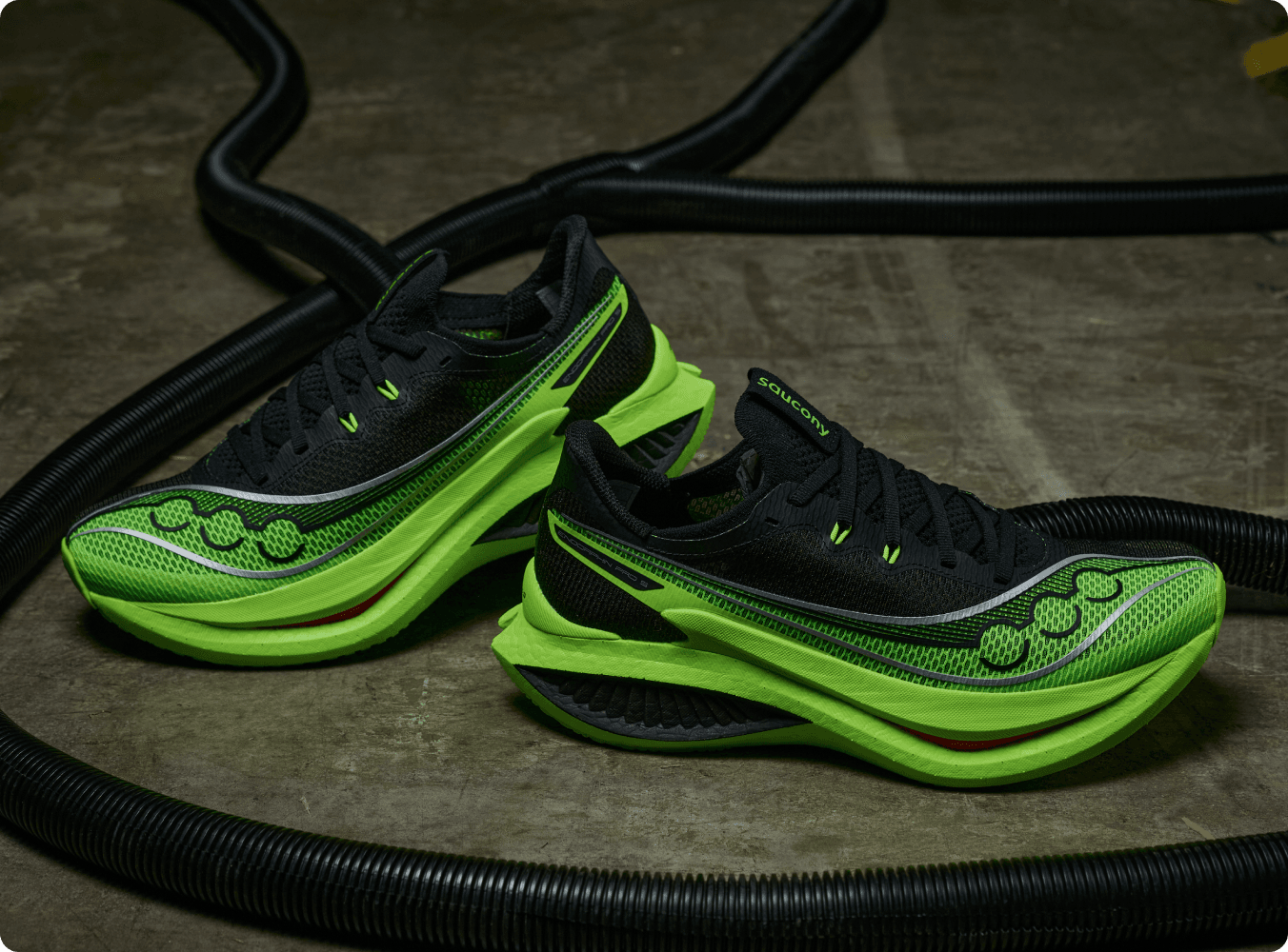 A pair of bright green and black Saucony running shoes beside gym equipment.