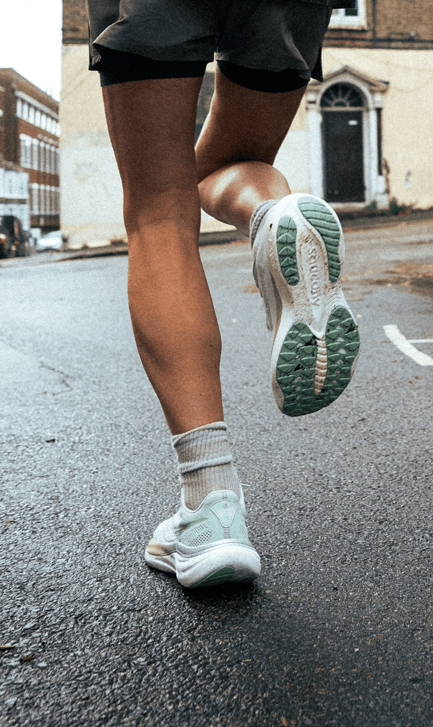Two runners' legs and Saucony running shoes mid-stride on a wet city street.