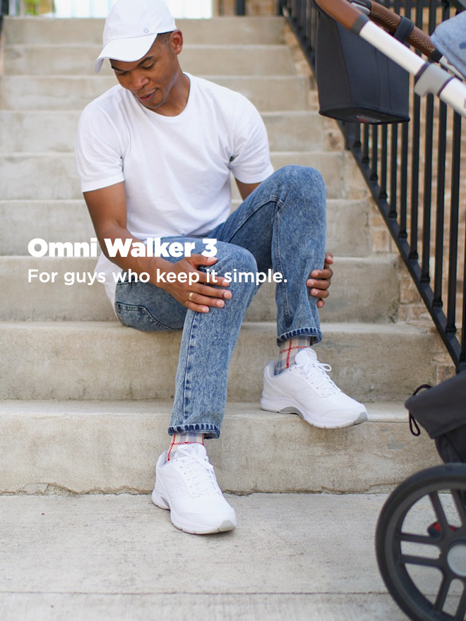 A guy wearing a white shirt, white hat and white Omniwalker shoes, sitting on some cement stairs next to a stroller.