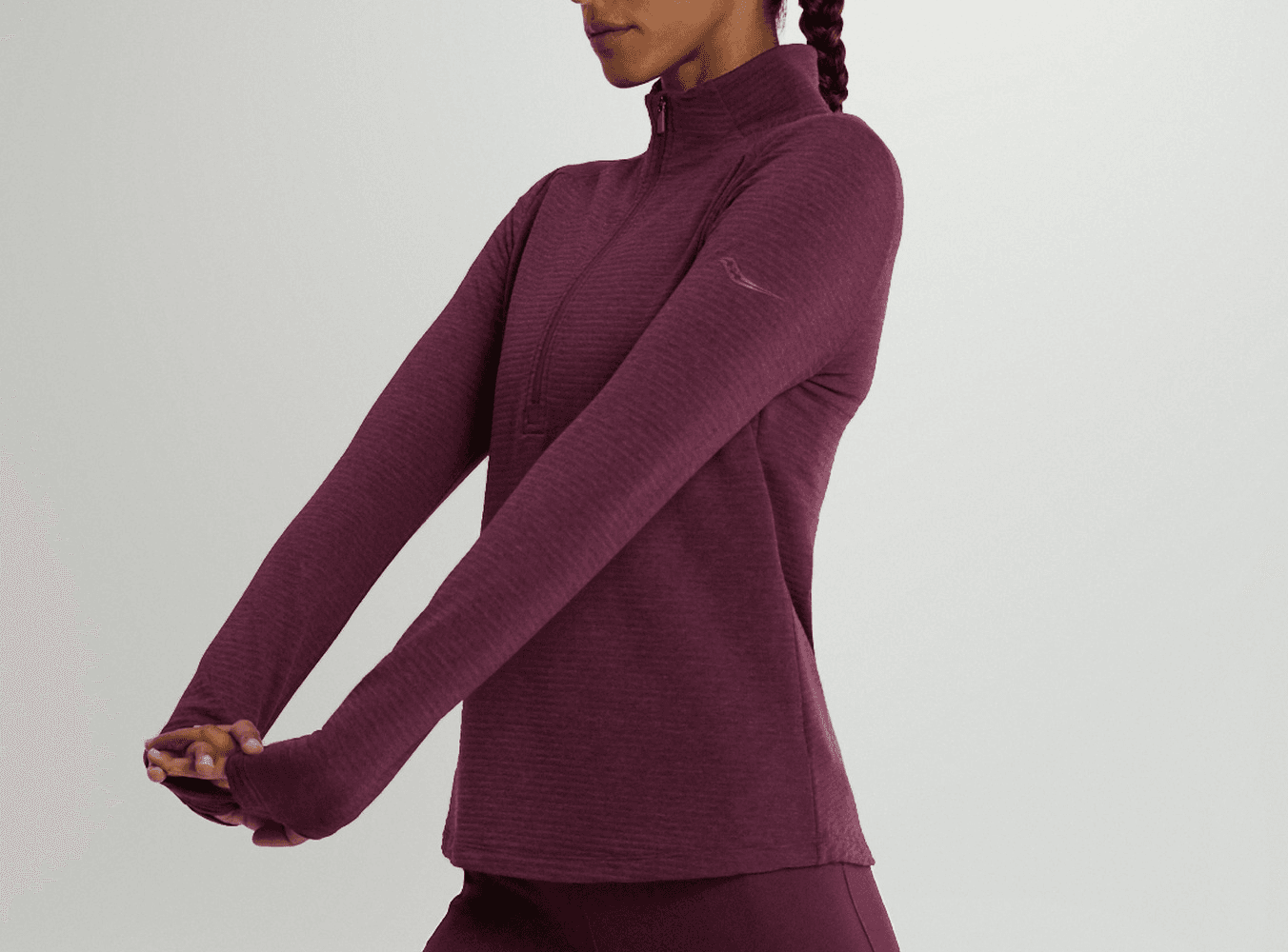 A runner wearing a maroon Saucony quarter-zip mid layer stretches before a winter run.