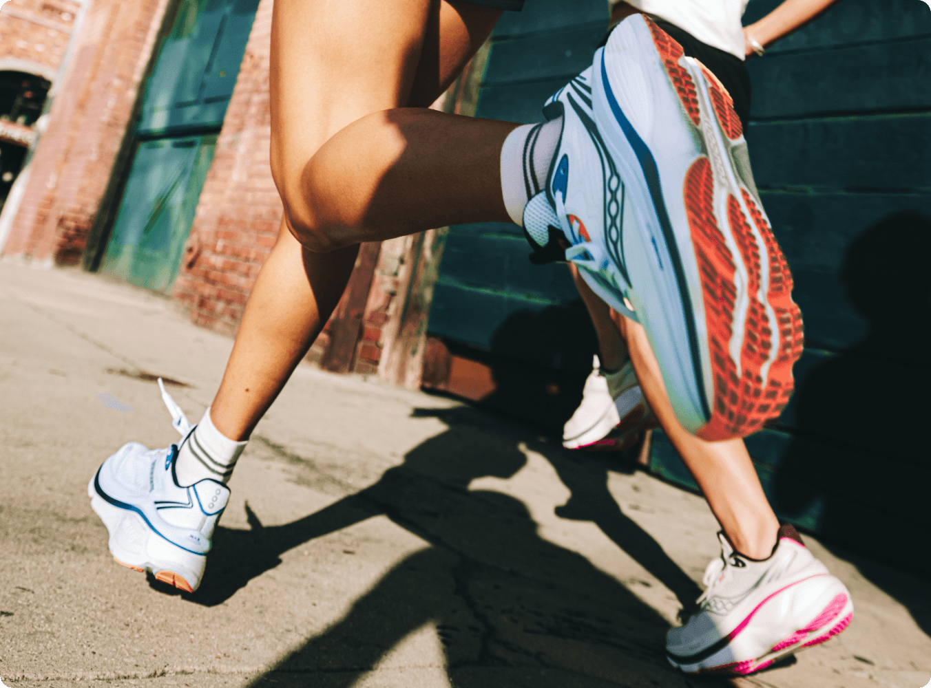 Two runners in athletic wear running together down a city alley.
