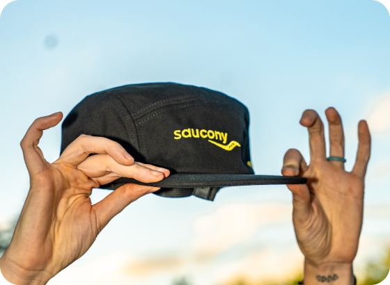 A black hat with a green Saucony logo on it