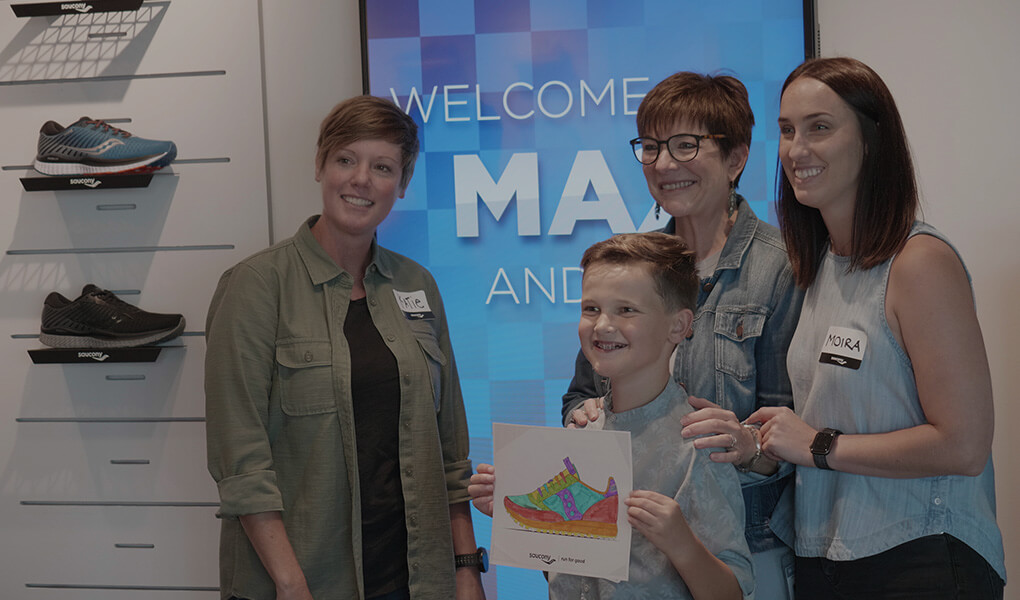 A proud kid stands with family showing off the shoe they designed.