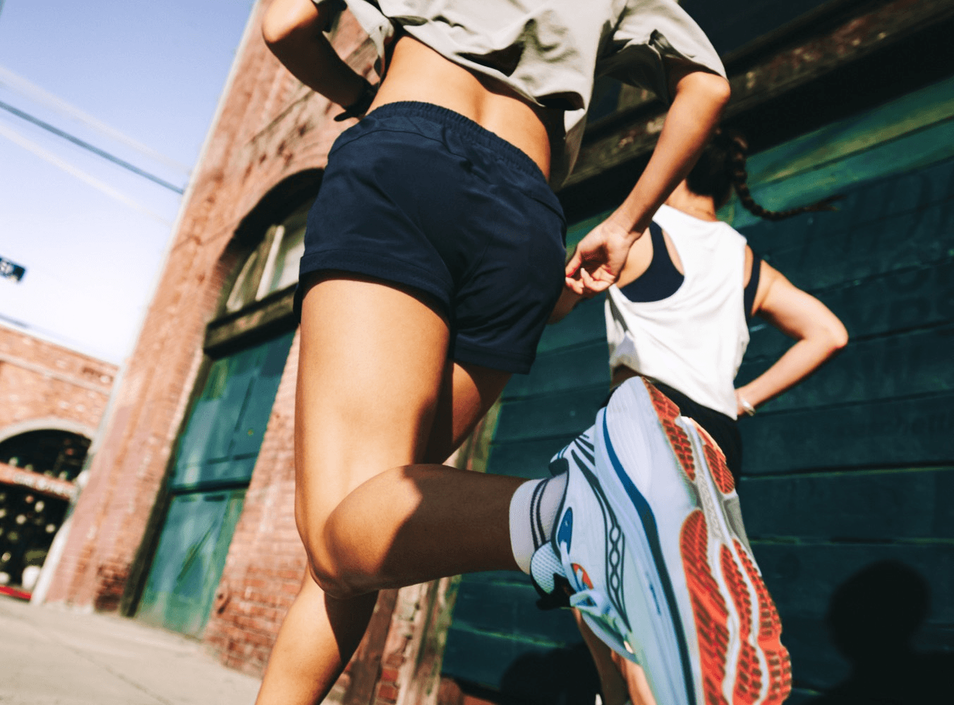 Two runners in athletic wear running together down a city alley.