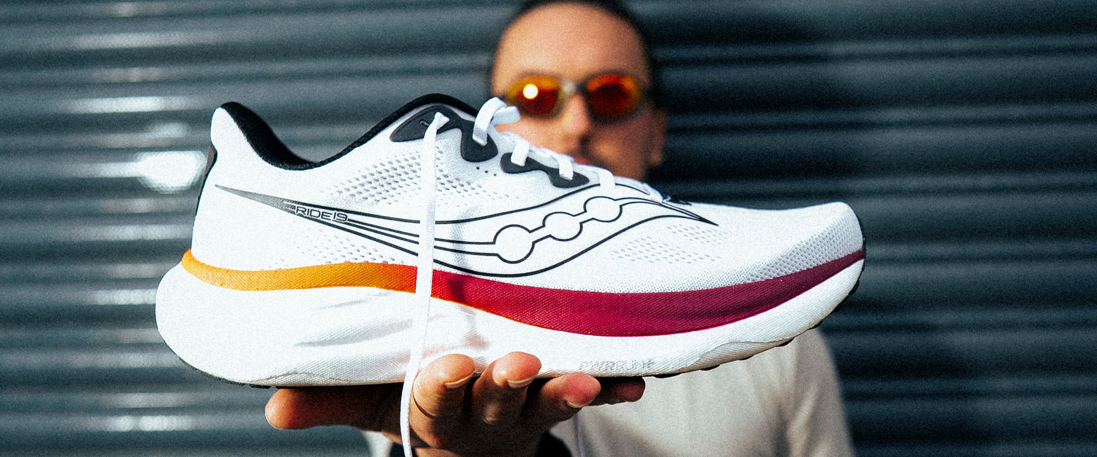 A person holding up a white Saucony shoe to the camera