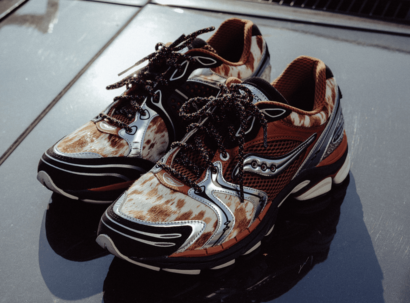 Close-up of brindle cow-print Saucony Space Cowboy running shoes on a car hood.