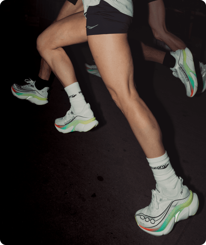 A picture of a person running on a track, at night using flash photography, wearing Saucony Endorphin Elite 3 shoes in the White | Multi colorway.