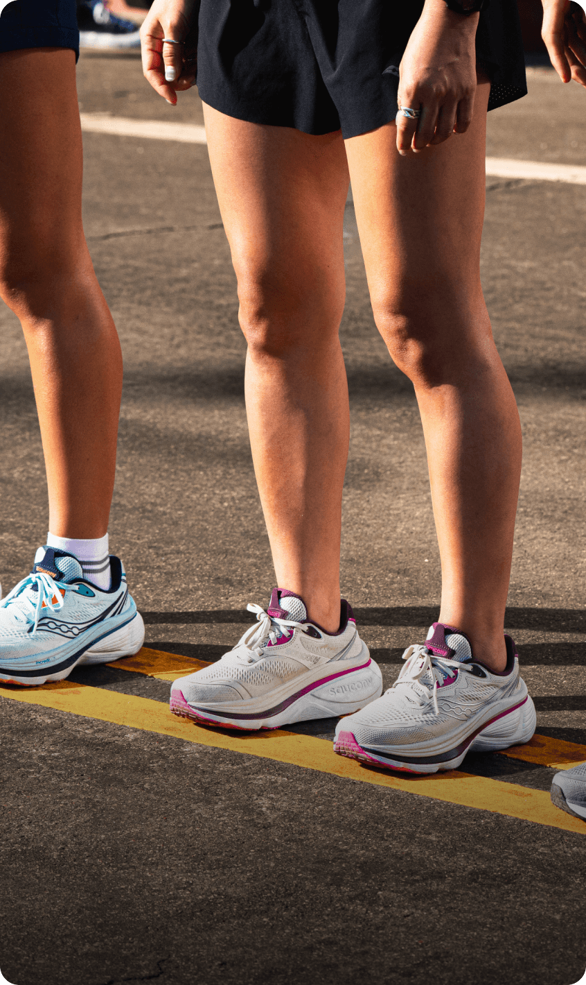 Three runners standing at a starting line wearing different colorways of Saucony running shoes.