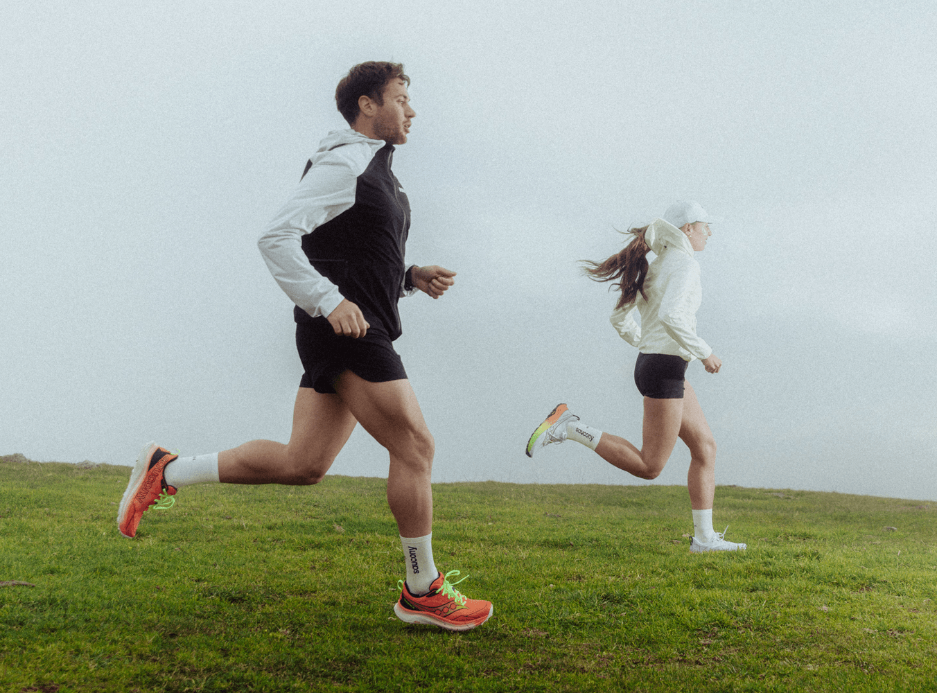 Two runners in Saucony shoes running along a grassy, foggy trail.