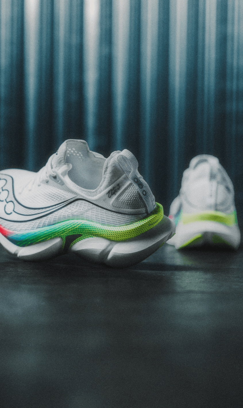 A pair of white Saucony running shoes with a rainbow gradient outsole.
