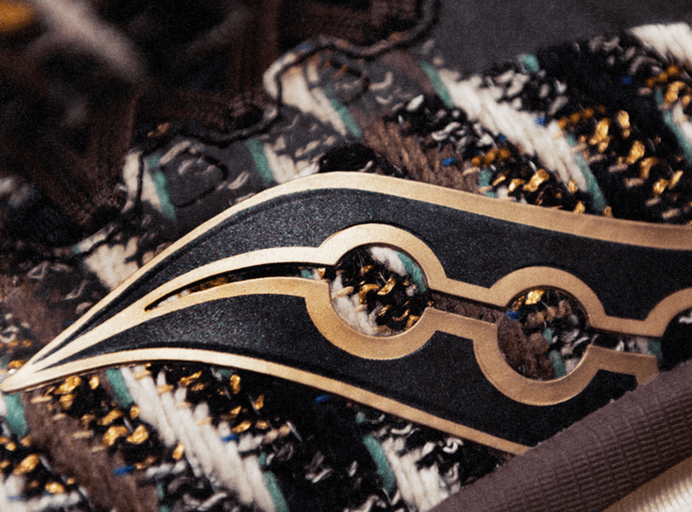 Close-up of the Saucony Sweater Weather shoe's gold wing logo on knit earth-tone fabric.