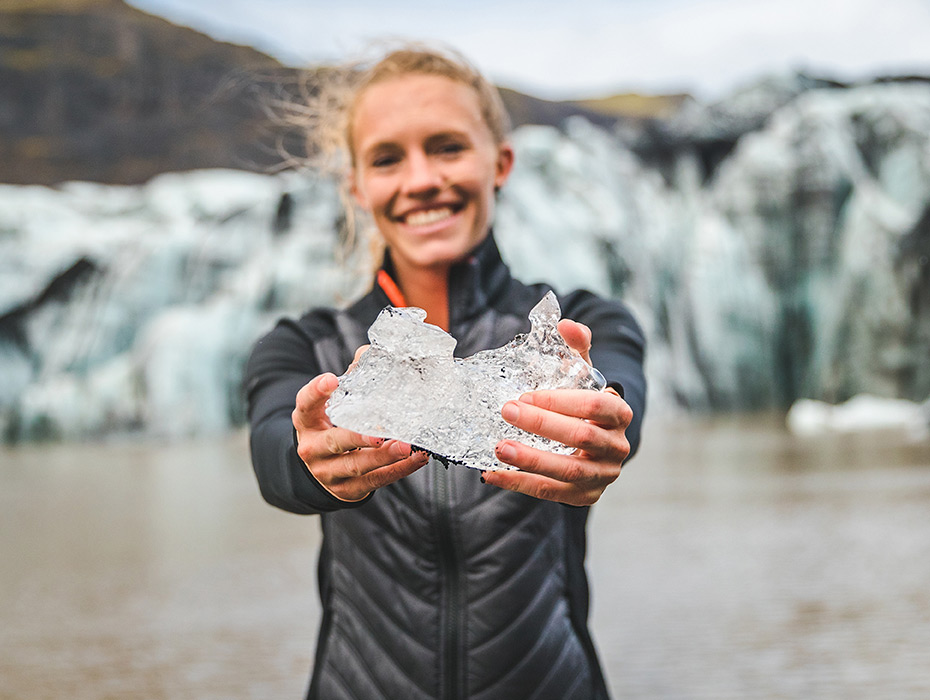 Female holds a piece of ice while standing in front of a glacier.