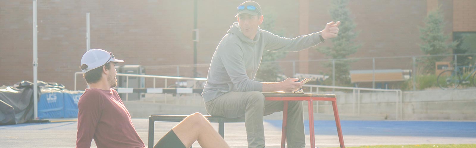 Track Club Coach Tim Broe giving tips sitting on a bench to a fellow runner.