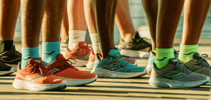 The feet of multiple runners all wearing Saucony running shoes in different colors outside.