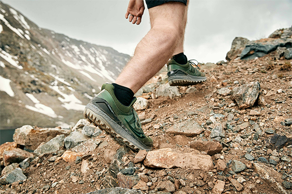 A shot of green Xodus ISO 3s in use. Wearer is climbing up a rocky dirt hill.