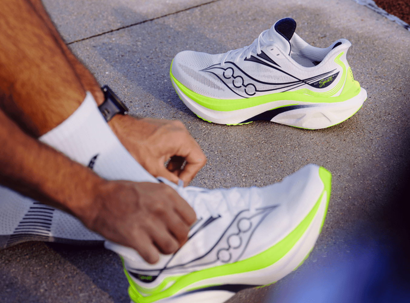 Runner tying the laces of the Saucony Endorphin Speed 6 next to a second pair on pavement.