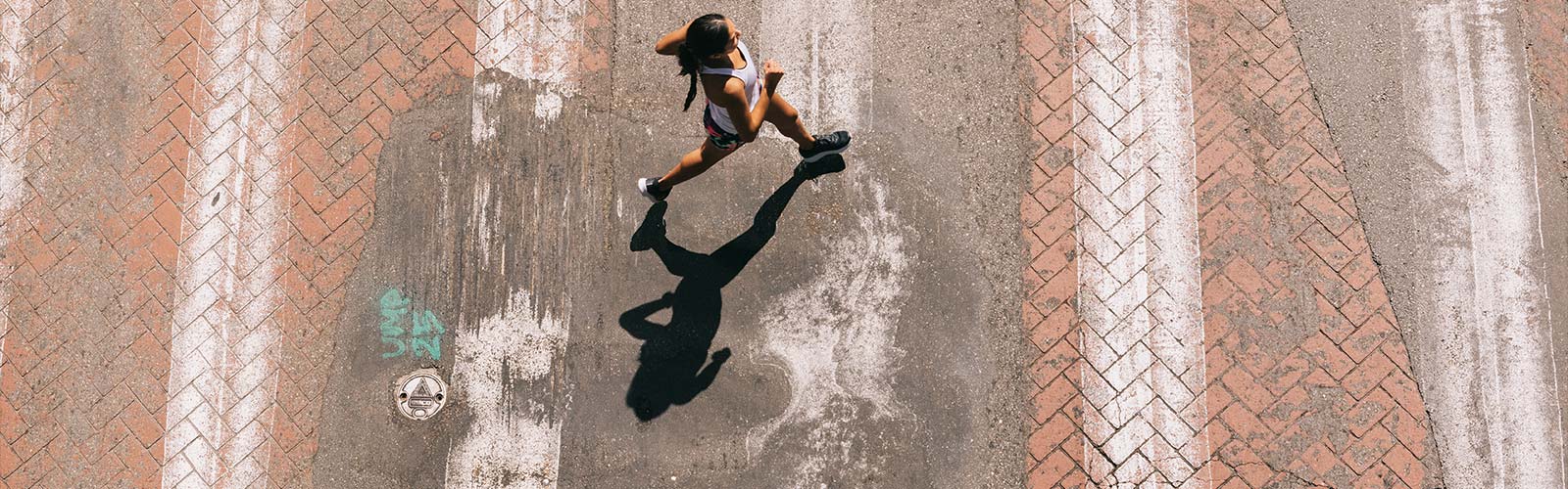 Top down view of a woman running on a brick and concrete road with white vertical lines.