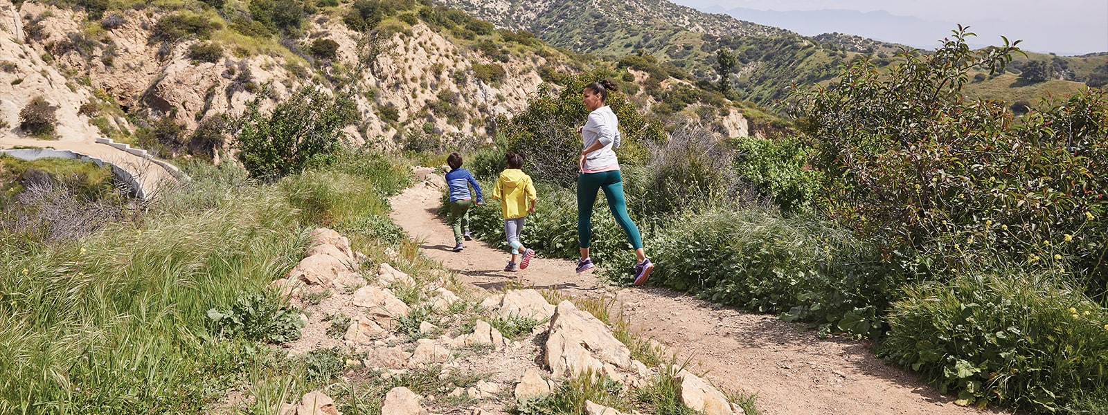 A mom and two kids going for a run on a trail