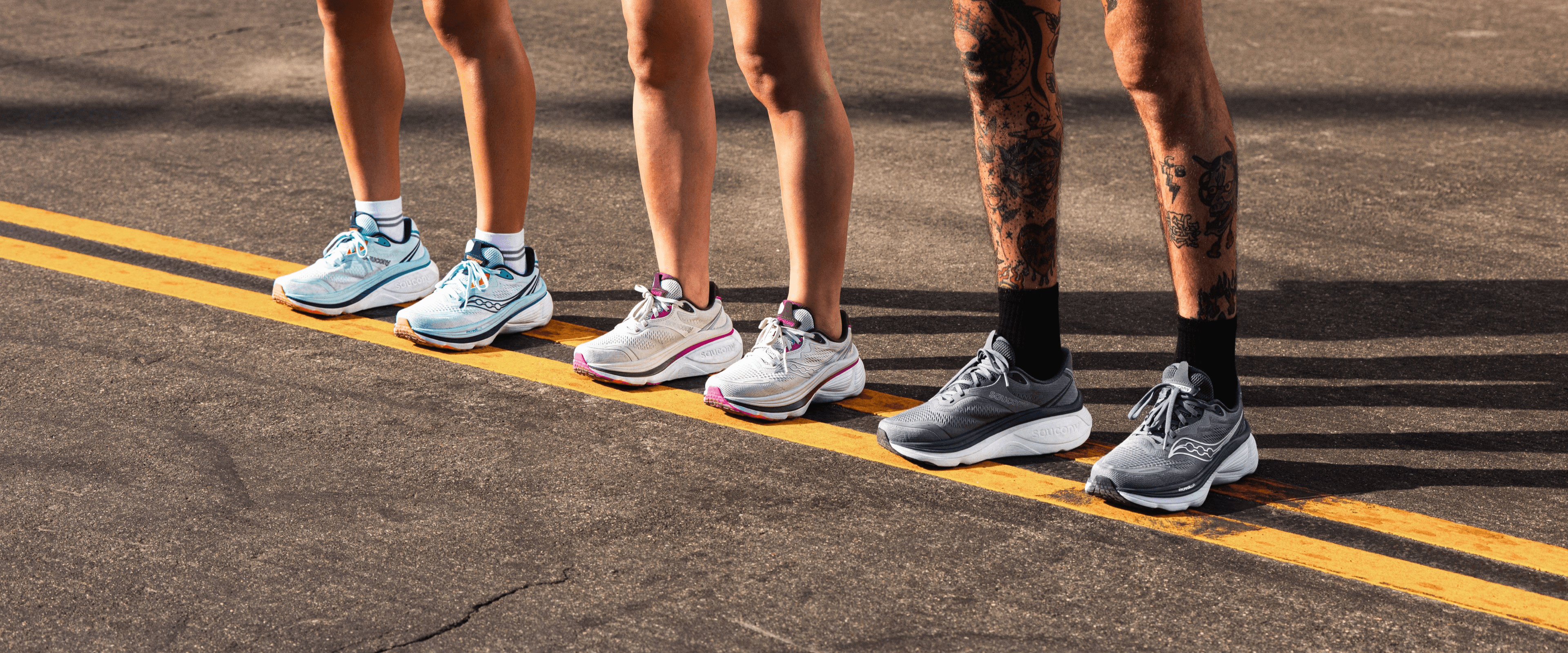 Three runners standing at a starting line wearing different colorways of Saucony running shoes.