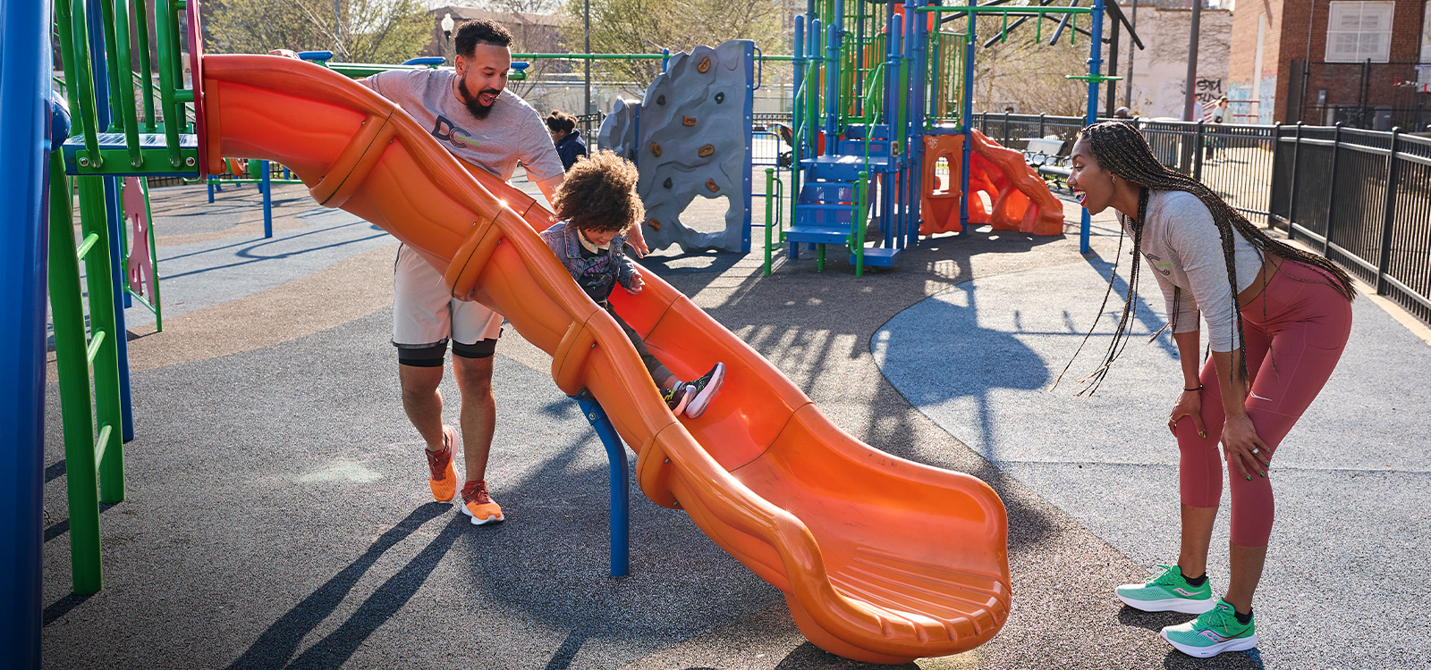 Parents in a playground and a child going down a slide.