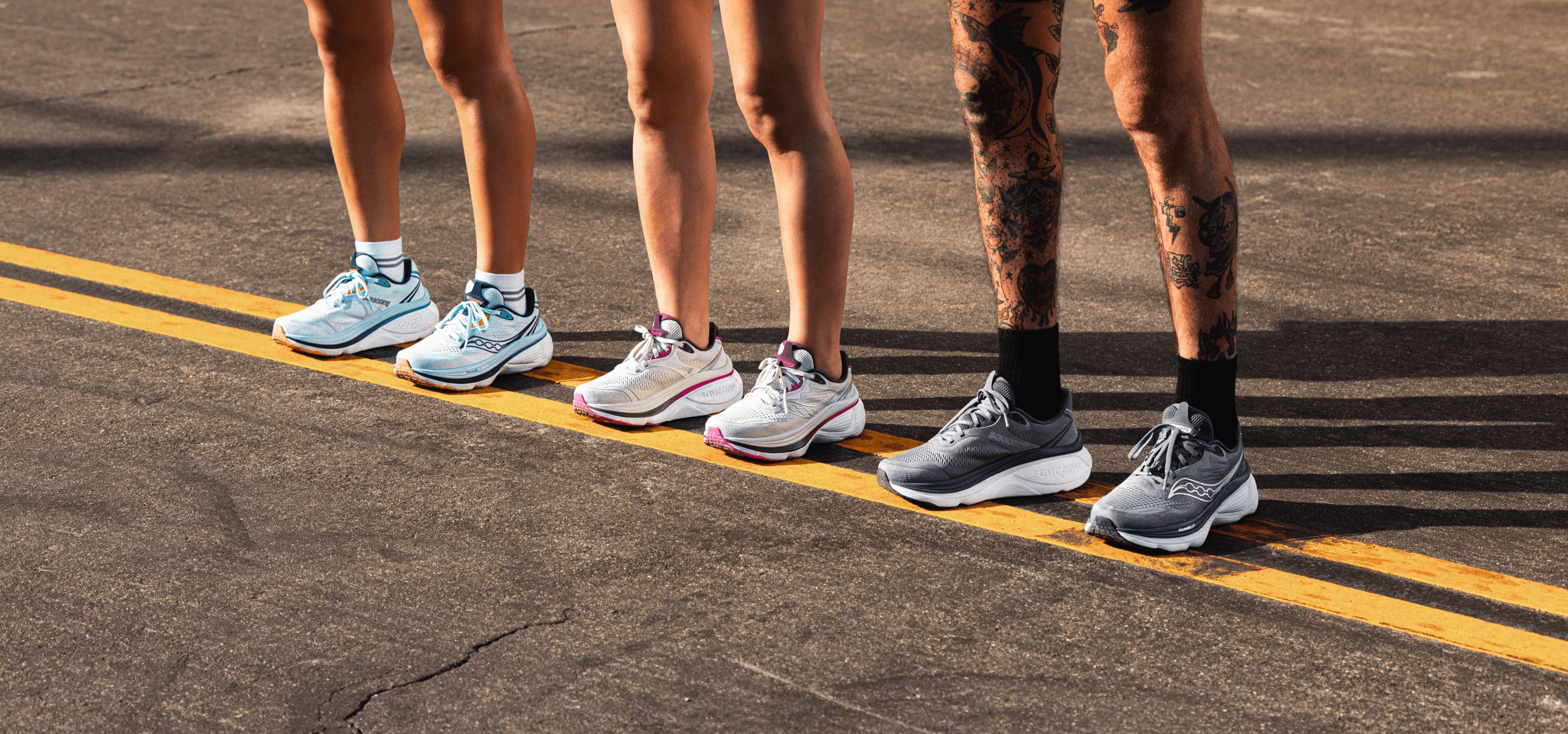 Three runners standing at a starting line wearing different colorways of Saucony running shoes.
