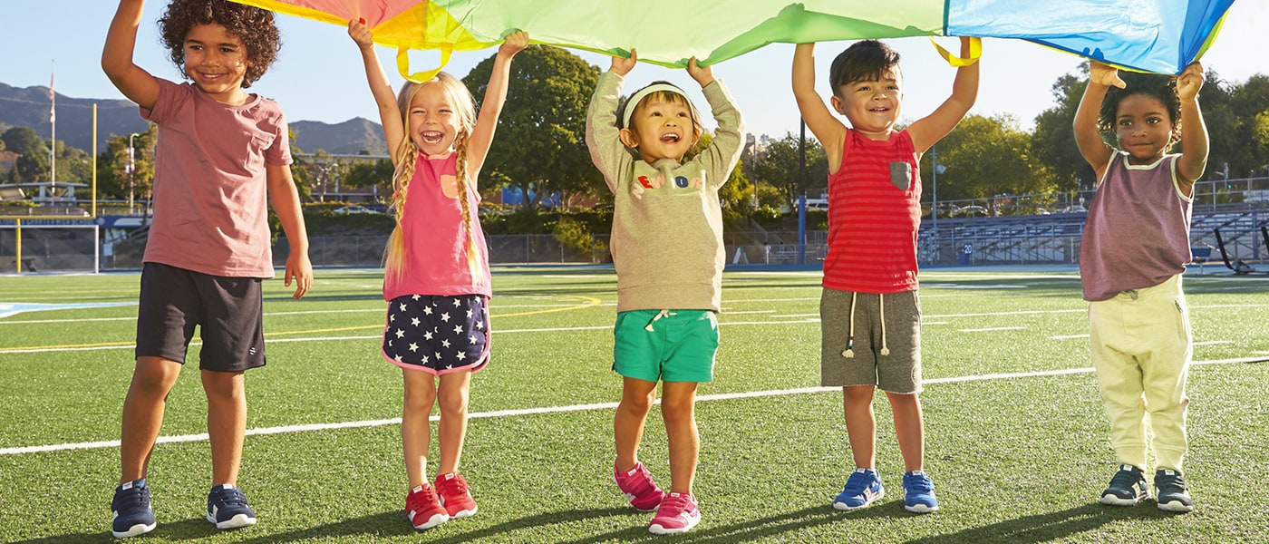 Kids smiling and playing parachute, all wearing Saucony Jazz Riff shoes.