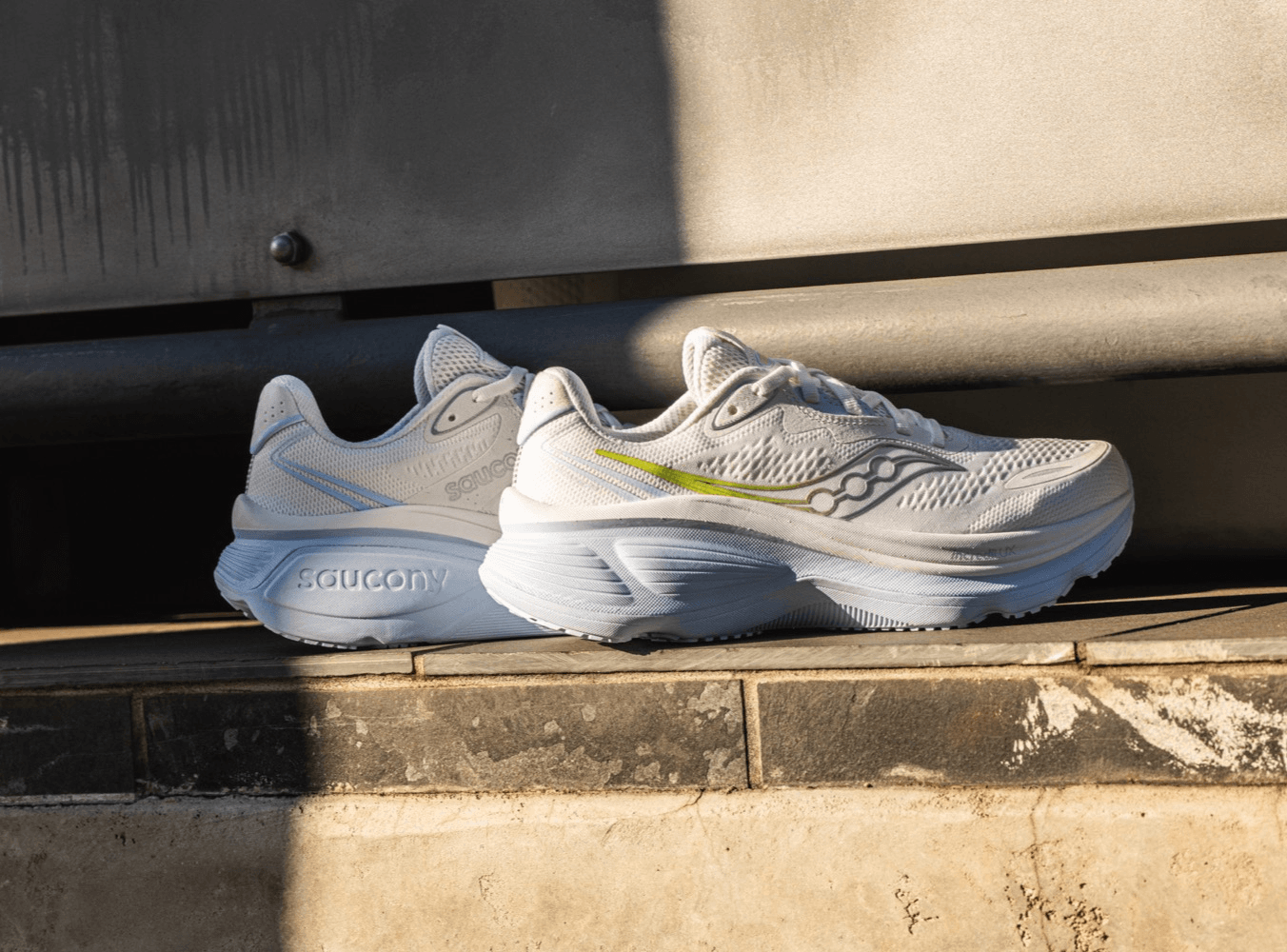 A pair of white and blue Saucony running shoes resting on a ledge in the sunlight.