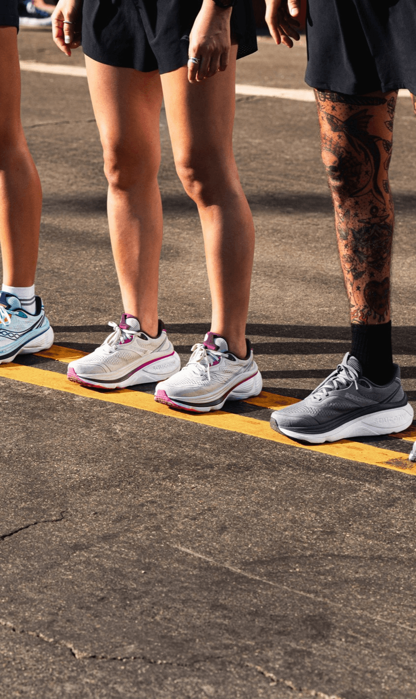 Three runners standing at a starting line wearing different colorways of Saucony running shoes.
