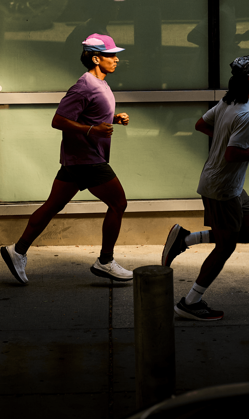 Three runners mid-stride on a city sidewalk past a glass building.